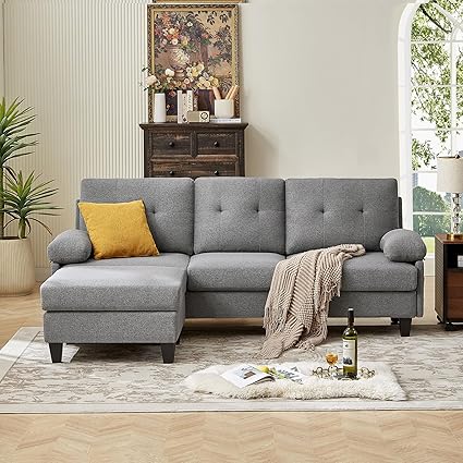 A dark grey convertable sectional sofa with a chaise on the left side, placed in a living room setting with decorative pillows, a rug, and a side table in the background.