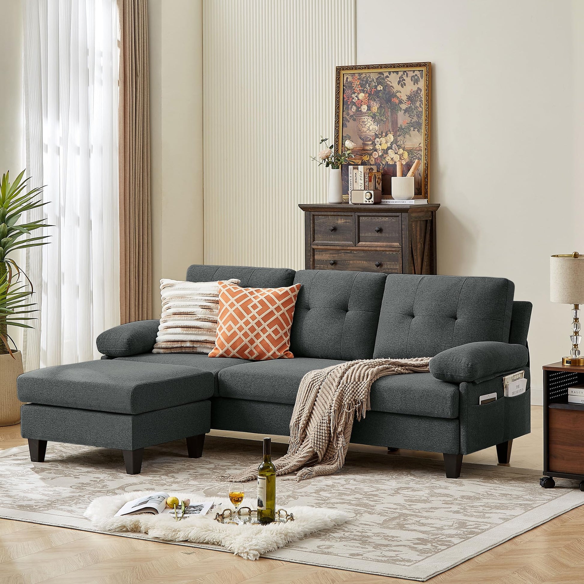A dark grey convertable sectional sofa with a chaise on the left side, placed in a living room setting with decorative pillows, a rug, and a side table in the background.