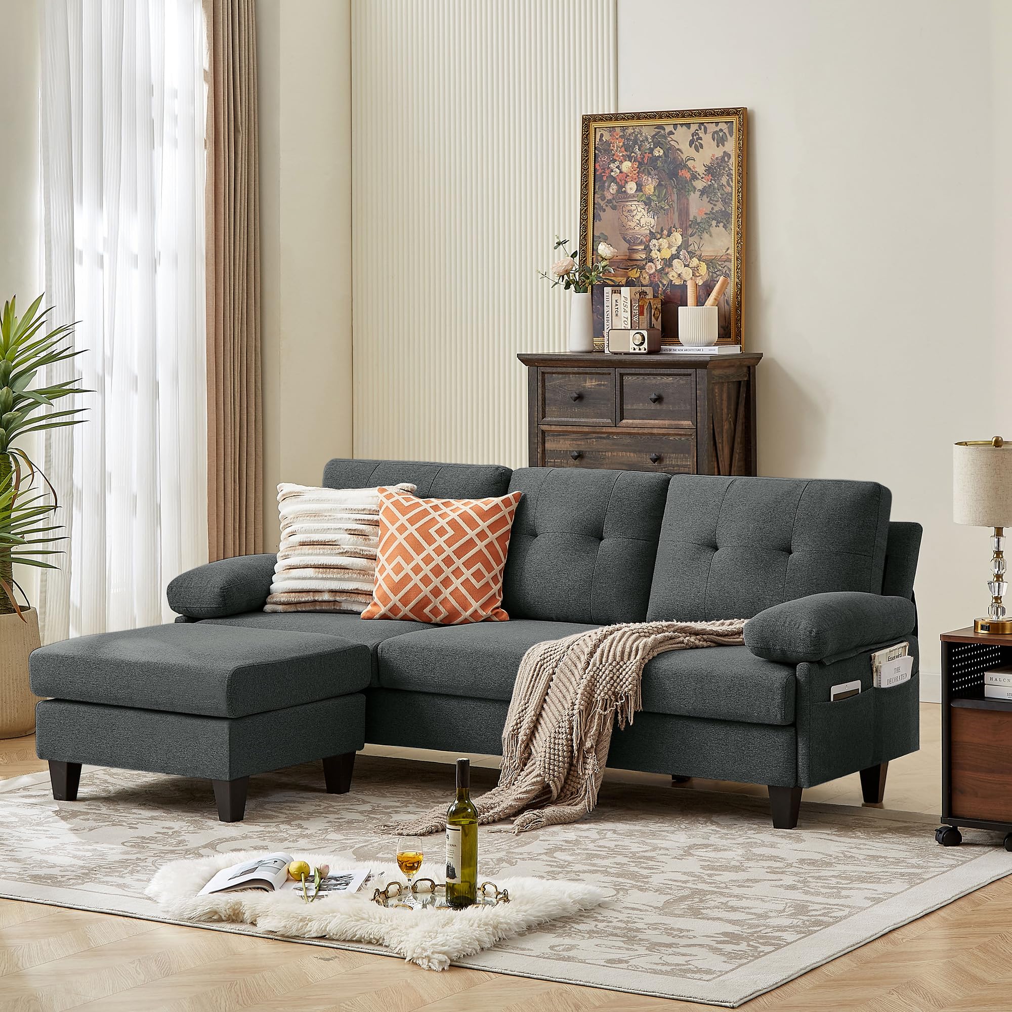A dark grey convertable sectional sofa with a chaise on the left side, placed in a living room setting with decorative pillows, a rug, and a side table in the background.