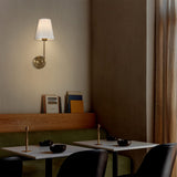 Hardwired Wall Sconce with Flared Shape White Textile Shade Curved Arm and Antique Brass Finish Metal Base